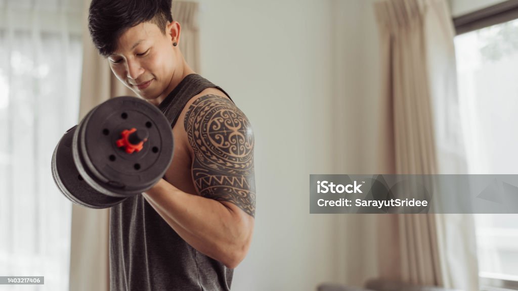 Fit man doing arms exeise at home. Young man doing biceps curl with dumbbells in living room at home. Domestic Life Stock Photo