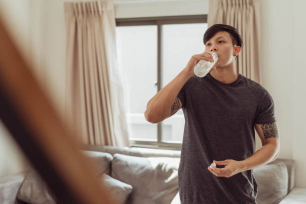 istock Fit man drinking water and take a break exercising at home. Young asian man resting after workout at home. 1403217411