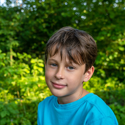 The face of a smiling boy on a blurred background of trees. Portrait of a 9 year old boy in a blue t-shirt in the garden