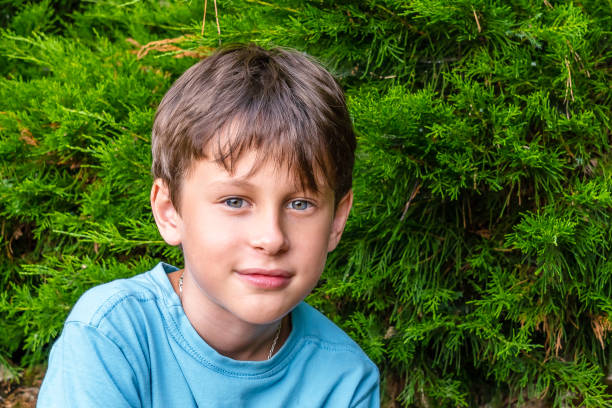 A 9-year-old boy smiles skeptically while looking at the camera. Portrait of a white Eastern European boy in the park