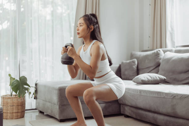 Young woman exercising at home. Asian healthy woman in sportwear doing squat exercise at home. Home exercise. Young woman exercising at home. Asian healthy woman in sportwear doing squat exercise at home. Home exercise. SQUATS stock pictures, royalty-free photos & images