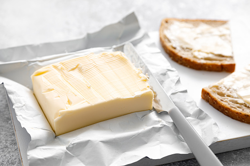 Block of butter with butter knife in a open pack.  Buttering bread