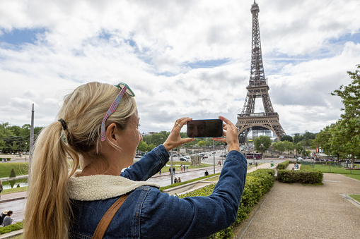 She uses her smart phone to text message and taking pictures of the famous place. Paris, France.