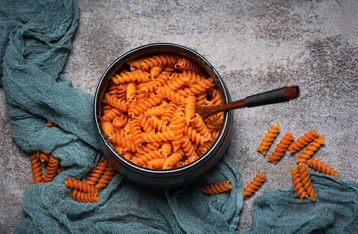 Italian orange spiral pasta, dry, uncooked in a black ceramic dish on gray background. Healthy organic gluten-free paste. Top view