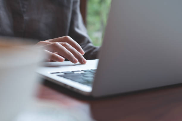 istock Woman hand using laptop computer on wooden table at home, searching information on web, browsing the internet, work from anywhere 1403225834