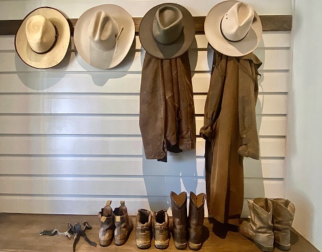 Horizontal still life of country style cowboy boots jackets and hats on wood bench & wall on rural horse property Australia