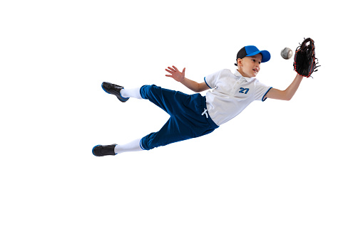 Little beginner baseball player in sports uniform playing baseball isolated on white background. Concept of sport, achievements, competition. School age boy learning to play baseball