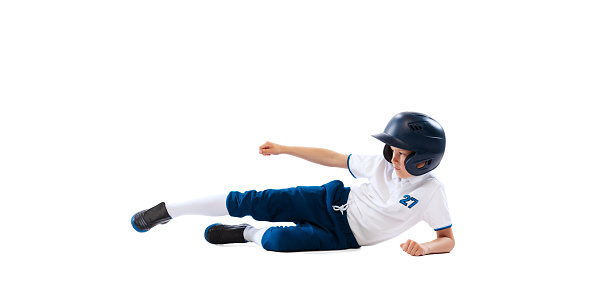 Little beginner baseball player in sports uniform playing baseball isolated on white background. Concept of sport, achievements, competition. School age boy learning to play baseball