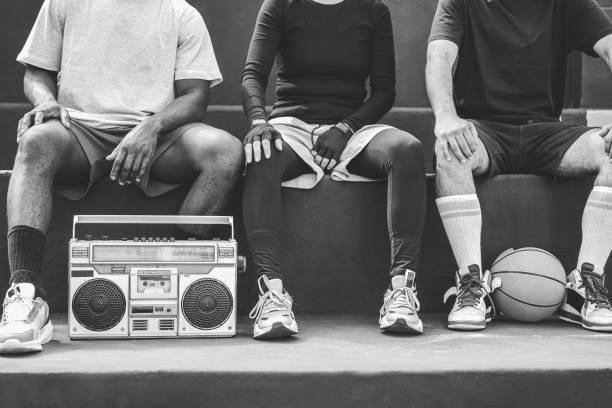 Group of young african people listening music outdoor after basketball match - Focus on boombox stereo - Black and white editing stock photo