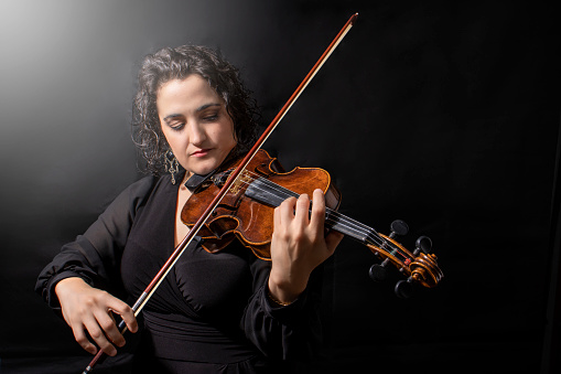 Front view of aged 40-44 years old who is beautiful with brown hair caucasian young women violinist standing in front of white background wearing pants who is laughing and holding violin