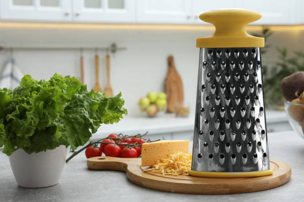 Grater, cheese and vegetables on table in kitchen