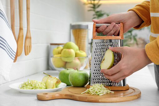 Woman grating fresh green apple at kitchen counter, closeup