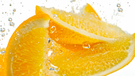 Close-up of orange slices falling into water against white background.