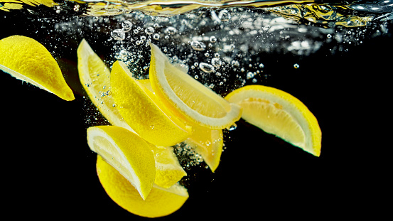 Close-up of lemon slices falling into water against black background.