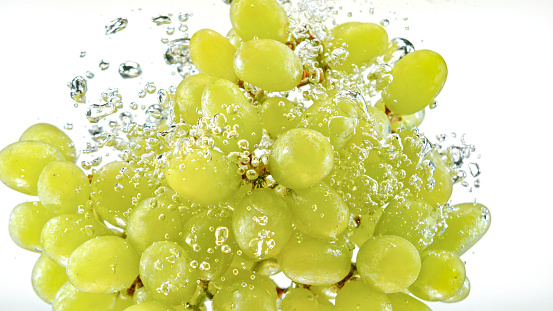 Close-up of grapes falling into water against white background.