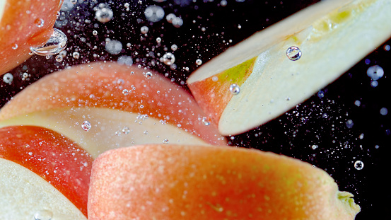Close-up of apple slices falling into water against black background.
