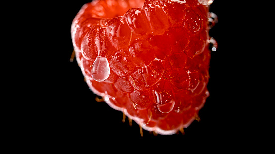 Close-up of raspberry with water drop against black background.