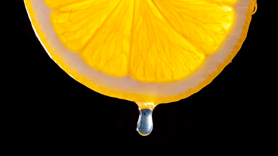 Close-up of orange fruit slice with water drop against black background.