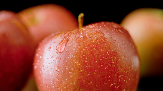 Close-up of apple fruit with water drops against black background.