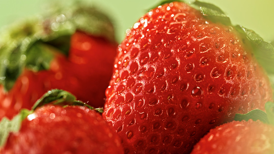 Close-up of water drops on strawberries against green background.