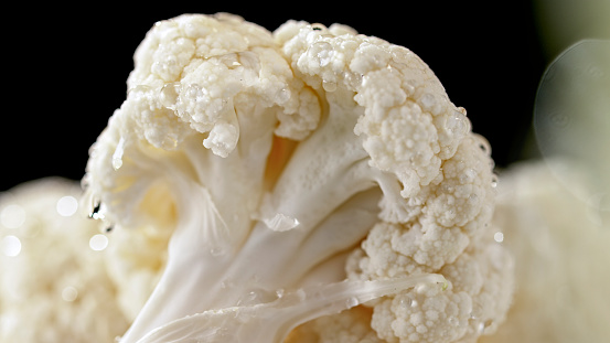 Close-up of cauliflower with water drops against black background.