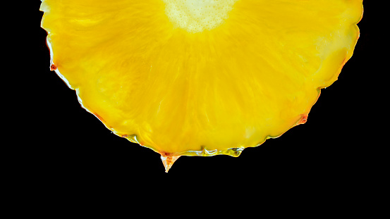 Close-up of pineapple fruit slice with water drop against black background.