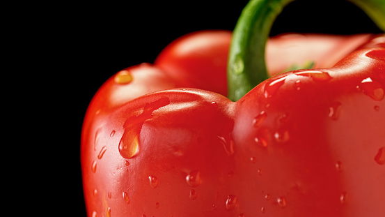 Close-up of red bell pepper with water drops against black background.