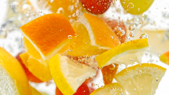 Close-up of fruit slices falling into water against white background.