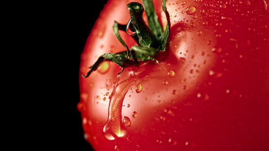 Close-up of fresh cherry tomato with water drops against black background.