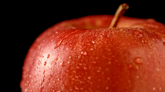 Close-up of apple with water drops against black background.