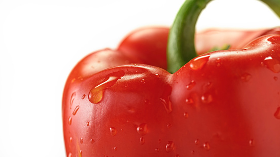 Close-up of red bell pepper with water drops against white background.