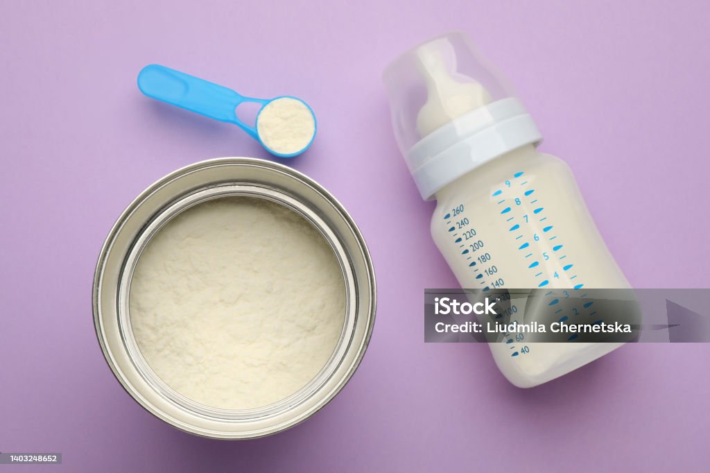 Feeding bottle with infant formula and powder on violet  background, flat lay Infant Formula Stock Photo