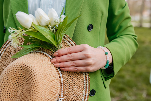 Close-up of a young woman in a green suit holding snowdrop flowers and a hat.