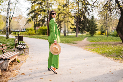 Profile of a beautiful young woman wearing green suit and a hat in a park.