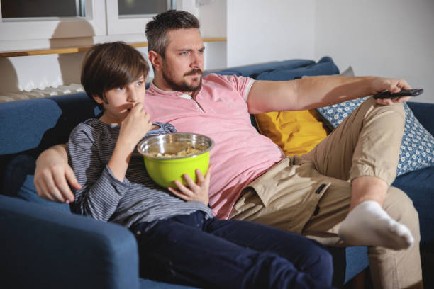 istock Serious man sitting on the sofa with his son and watching TV 1403250473