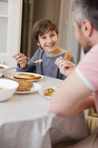 istock Boy sitting at the dining table, smiling at his father and having lunch 1403250496
