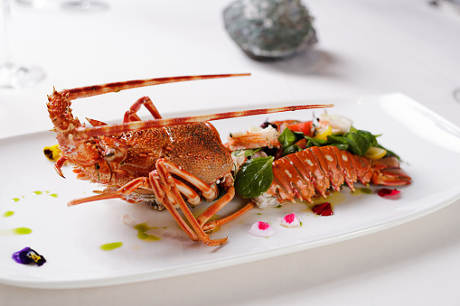 Lobster serving in fine dining on a rectangular plate, cut in half and filled with spinach and vegetables