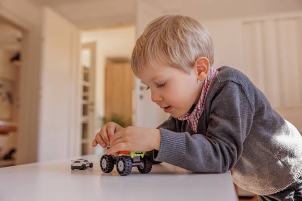 istock Blond boy playing at the table with toy cars, focused on assembling elements 1403252536