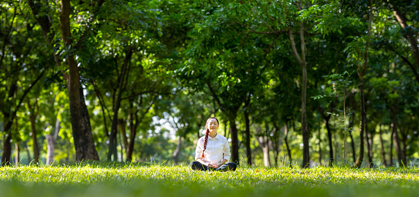 Woman relaxingly practicing meditation in the forest to attain happiness from inner peace wisdom with beam of sun light for healthy mind and soul