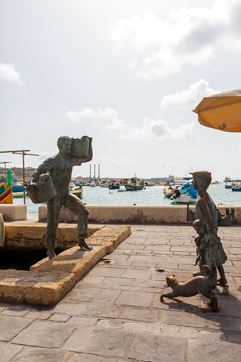 Marsaxlokk, Malta - Sep 25, 2021: Bronze statue in Marsaxlokk harbor of a fisherman returning home to his son, daughter and the cat