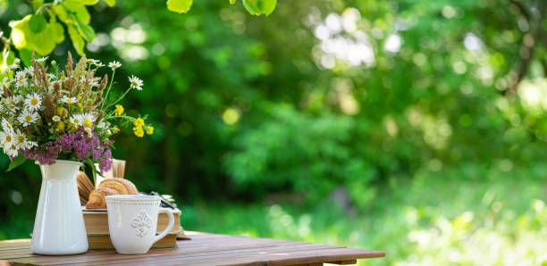 牧草地の花束、クロワッサン、紅茶やコーヒー、サマーガーデンのテーブルの上の本。庭で休んだり、本を読んだり、朝食を取ったり、自然の中での休暇をコンセプトにしたり。裏庭の庭の� - afternoon tea 写真 ストックフォトと画像