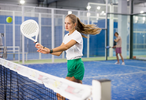 Portrait of a confident fifteen-year-old girl tennis player engaged in the popular sport of padel with a racket indoors