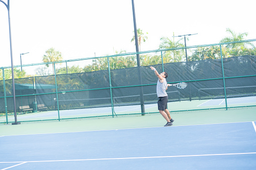 A male player practising serve at tennis court on a sunny day. Long shot.