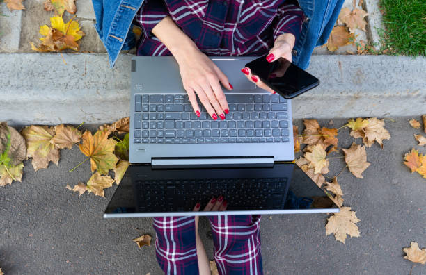 Student studying outdoors. Top view of modern girl sitting on the grass under with laptop and smartphone in park. Hands on keyboard. stock photo