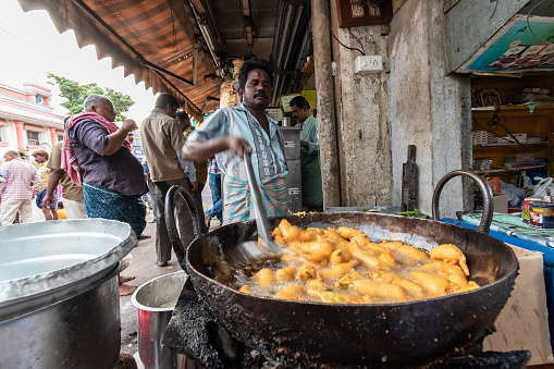 Tirupati, Andhra Pradesh, India - September 2018: An Indian street food vendor deep frying snacks in oil at his stall in the market.
