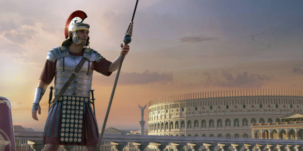 A Roman Soldier Standing On A Balcony In Full Armour Holding a Spear With Buildings Of Classic Rome In Background A male roman soldier in full uniform, armour, helmet, carrying a sword and dagger, standing and looking way from the camera, holding a spear - pilum near to a shield. The grand classical buildings of Ancient Rome, including the Colosseum are visible in the background at sunset. roman centurion stock pictures, royalty-free photos & images