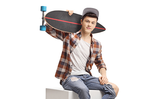 Teenager sitting and holding a longboard isolated on white background