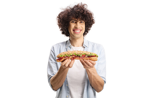 Young man with curly hair holding a baguette sandwich and smiling isolated on white background