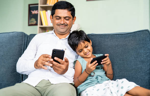 istock focus on kid Young father and kid by leaning busy using mobile phone while sitting on sofa - concept of technology, social media and internet 1403268890