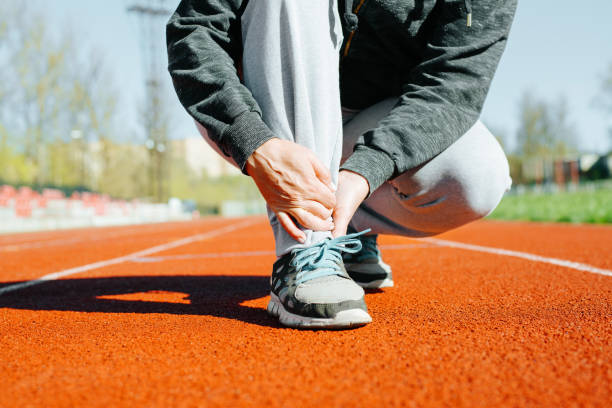 Sports injury while exercising outdoors. Close-up of woman suffering from pain in tendons of lower leg and foot, muscle sprain due to intense running training in stadium stock photo